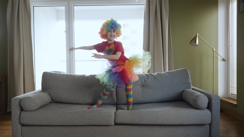 Clown Playing in Living Room. Funny Happy Little Girl in Clown Costume Dancing and Jump on Couch at Home. Love Lifestyle Home. Slow Motion. 