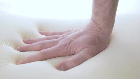 Hand is touching the memory foam mattress of a modern bed.