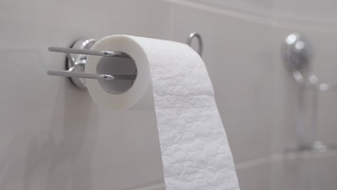 Slow motion: toilet paper is unwound which is hanging on the wall in the bathroom.