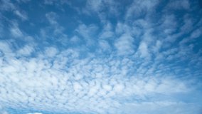 Seamless time lapse of white cirrocumulus clouds that flow continuously in loop from right to left in the blue sky