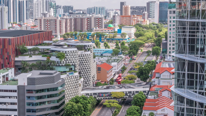 Singapore skyline with Victoria street and National Library aerial timelapse. Green trees on the road with traffic. Clouds on a blue sky