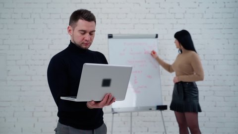 Young man and woman in the studio. Handsome man working on a laptop while woman is writing on a white board behind him.