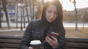 Beautiful woman use phone sitting on a park bench with coffee cup.