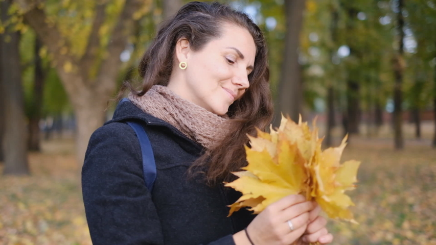 A young woman holds yellow autumn leaves in her hands.