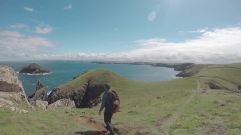 Man hiking on coastline path in Cornwall - Young man with backpack and hiking clothes on the cliffs over seashore in Cornwall, UK on a sunny day - Travel, nature and wanderlust concepts