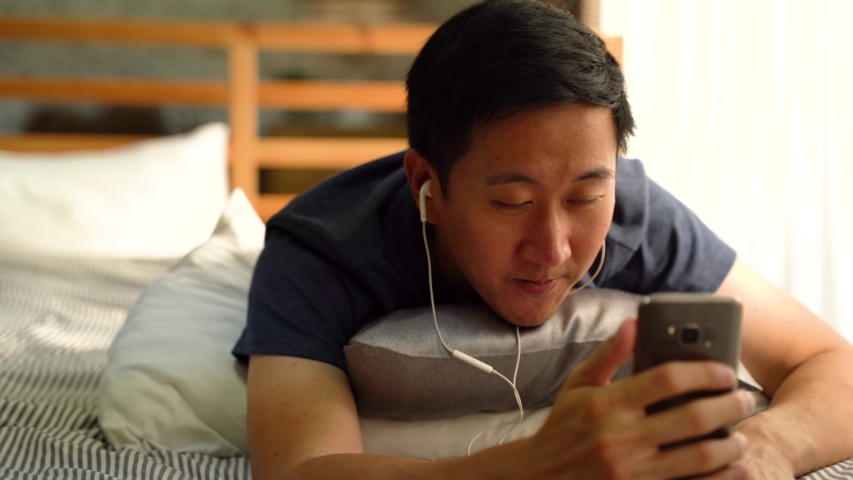 Portrait of happy 30s Asian man in casual clothing making facetime video calling with smartphone at home, waving at people on phone screen. Using conferencing meeting online app, social distancing Royalty-Free Stock Footage #1049301874
