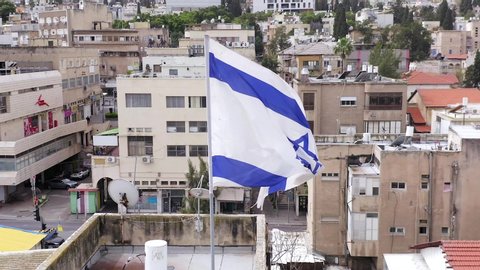Haifa, Israel - March 27, 2020: Corona Virus days, Israeli flag waving in the wind with Empty streets and closed shops at Haifa Talpiot food market, Aerial view.