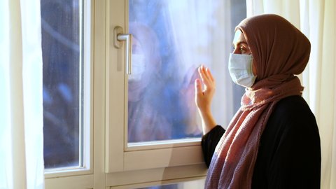 COVID-19 Pandemic Coronavirus Woman with hijab with wearing face mask looks out the window isolation. arab woman hijab. Muslim woman with hijab arab.