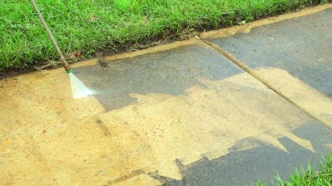 Dirty sidewalk being cleaned with water from a pressure washer