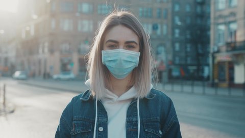 Portrait of a girl standing and putting on a protective mask on the street. Concept of health and safety life N1H1 covid19 coronavirus virus protection pandemic slow motion outdoor