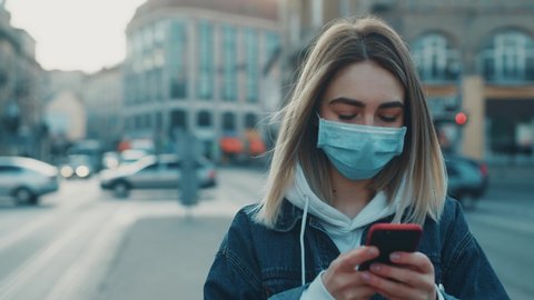 Portrait view of slender girl in protective mask on street using phone writing texting concept of health and safety life N1H1 covid19 coronavirus virus protection pandemic slow motion outdoor city