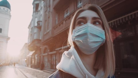 Extrime close up view of young blonde woman in protective mask stands in city street looks around sunset sunlight to the background covid19 corona virus protective pandemic city slow motion outdoor