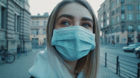 Extrime close up view of young blonde woman puts on protective medical mask looks around and goes out leves the frame shoot covid19 corona virus protection pandemic city slow motion outdoor