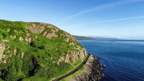 Causeway Coastal Route a.k.a Antrim Coast Road near Ballygalley Head mountain and resort in Northern Ireland, UK. One of the most scenic coastal roads in Europe. Aerial 4K flyby video. Sunrise light