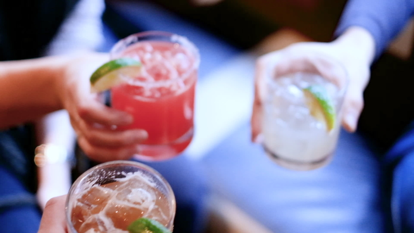 Friends toasting, saying cheers holding tropical blended fruit margaritas. Watermelon, tamarind, and lime drinks and cocktails. | Shutterstock HD Video #1049328481
