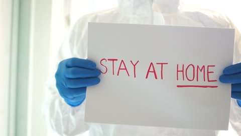 Man in a protective suit is holding a sign saying stay at home. Epidemic of coronovirus covid-19. Quarantine and self-isolation
