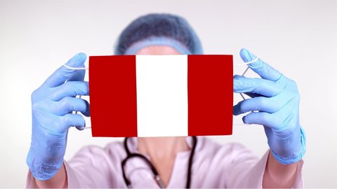close-up. Doctor in glasses, blue medical cap, gloves holds in hands medical mask with Peru flag. Physicians care, protection by state during coronavirus, global epidemic. Concept.