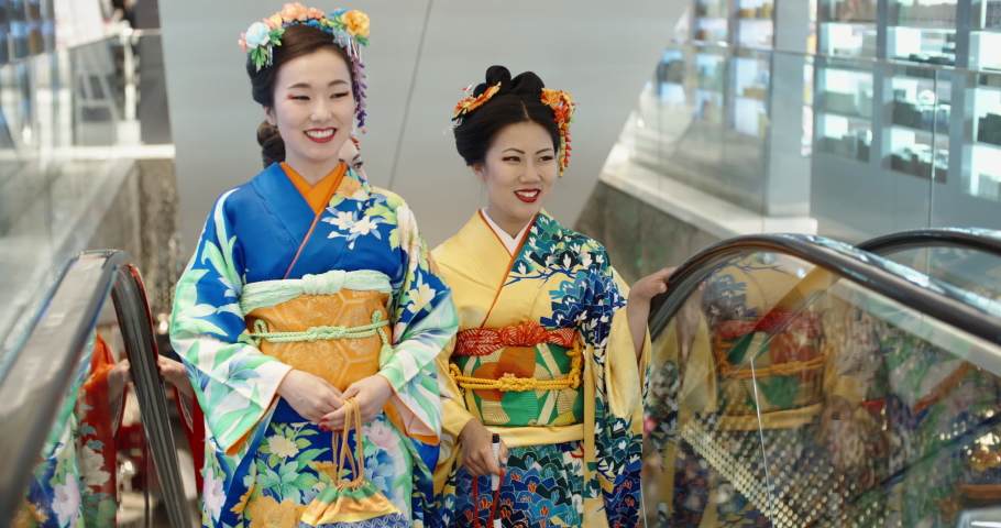 Three beautful japanese geishas in traditional kimono dresses walking in shopping cenre, standing in escalator and chatting - traditional culture in modern japan 4k footage