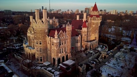 Flying over the Turrets and Red Tile Roof of a Castle at Golden Hour. Drone shot of Casa Loma Tourist Destination in Toronto Ontario Canada, Snowy Winter Sunset Light on Unique Old Mansion Home