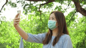 Asian woman wearing medical mask with video call smartphone of screen enjoying social distant in the green park.