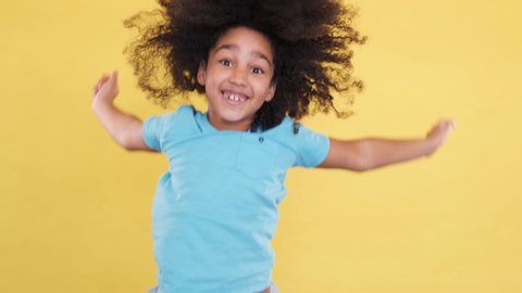 Happy and Joyful Little 5 years old Kid Jumping on yellow Background. She Smiling, Laughing and Feel Well. Playful Preschool Kid Have Fun Indoor. Rejoicing, Positive Feelings. Slow motion shoot.