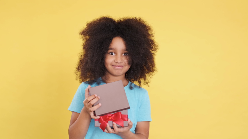 Surprised, Amazed African American Little Cutie with Lush Curly Hair. She Opens or Unpacking Gift. Emotions of Joy, Happiness. Receive A Surprise Gift. Birthday or Thanksgiving Day. Close Up.