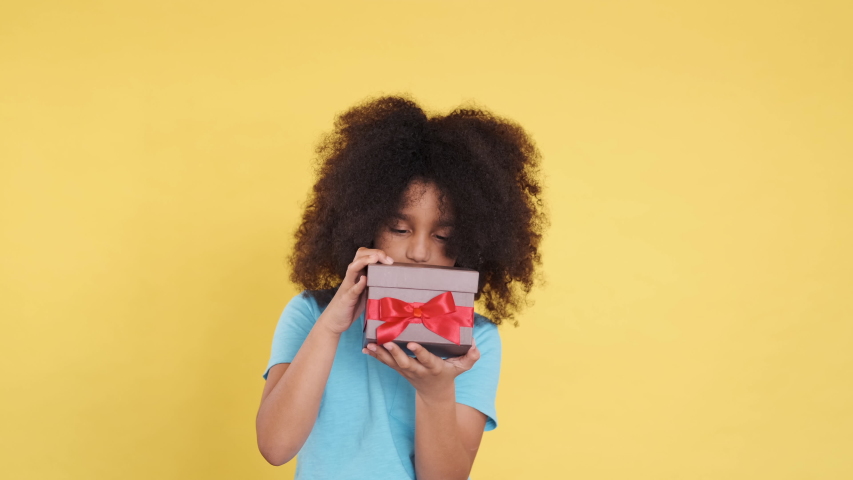 Frustrated, Disappointed Beautiful African American Little Cutie with Curly Hair. She Opens or Unpacking Gift. Unsatisfied, Angry, Unhappy Emotions. Isolated on Yellow Colourful Background. Close-Up.
