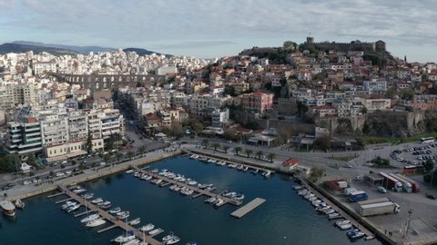 Drone flight over the city of Kavala in northern Greece, old town, houses with red roofs and medieval city wall, ancient aqueduct Kamares and marina with boats