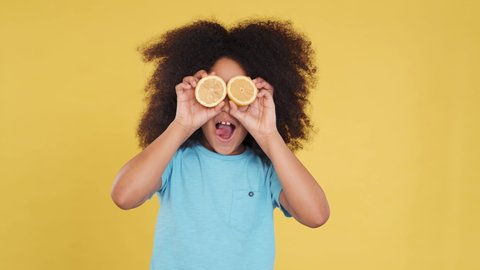 Funny Foolish Face of Small Dark-skinned Girl with Juicy Lemons. She Dancing with Fruits and Use it like a Glasses. Sticks out Tongue. Concept of Natural Organic Products, Healthy Food. Closeup.