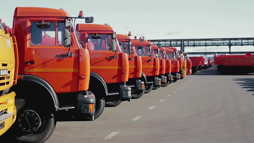 Row of new trucks standing on a concrete surface on blue sky background. Stock footage. Mechanical engineering and construction concept, newly built lorries. Royalty-Free Stock Footage #1049360755