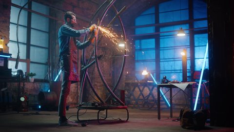 Handsome Male Artist Uses an Angle Grinder to Make Brutal Metal Sculpture in Studio. Hipster Guy Polishes Metal Tube with Sparks Flying Off It. Contemporary Fabricator Creating Abstract Steel Art.