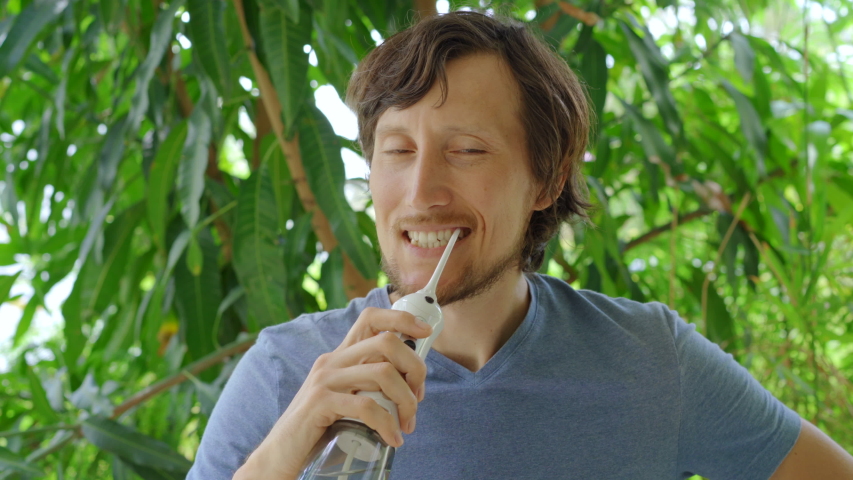 A young man uses a portable water flosser dental oral Irrigator to clean his teeth