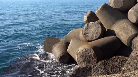 Amazing water splashing against sea shore, massive defensive constructions at the beach for preventing water flood. Sea pier fortification with powerful stone blocks of triangular shape