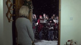 Carol Singers at Christmas Singing outside - Women opens front door -Snowing - View from Inside, Crane Shot - Stock Video Clip footage