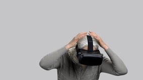 Old retired lady experiencing virtual reality and reacting expressively. Grey isolated background.