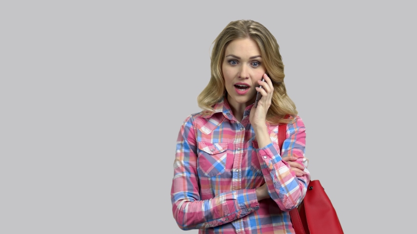 Emotional expressive young woman talking on phone. Glamour blond girl shocked and amazed, isolated on grey background.