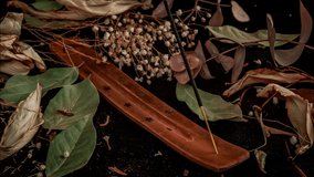 Time Lapse of stick holder and incense stick with leaves and flowers on black background.