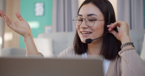Adult, smart and beautiful woman looking on laptop display and sitting at home working space with modern interior. Female in call center operator using headset and microphone