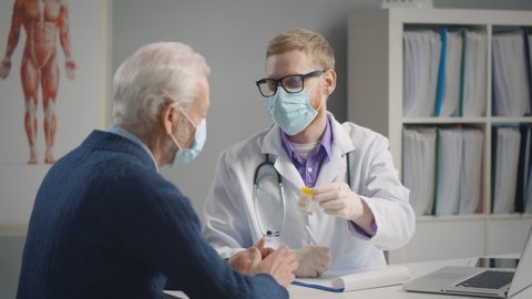 Elderly patient having flu visiting doctor wearing medical mask and having medicine prescribed against influenza. Physician seeing patients in facial masks to protect from covid-19 epidemic