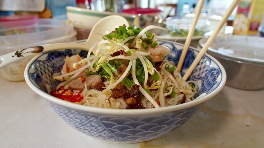 Pouring Pork Soup Broth Over a Bowl of Asian Noodles and Toppings in Slow Motion