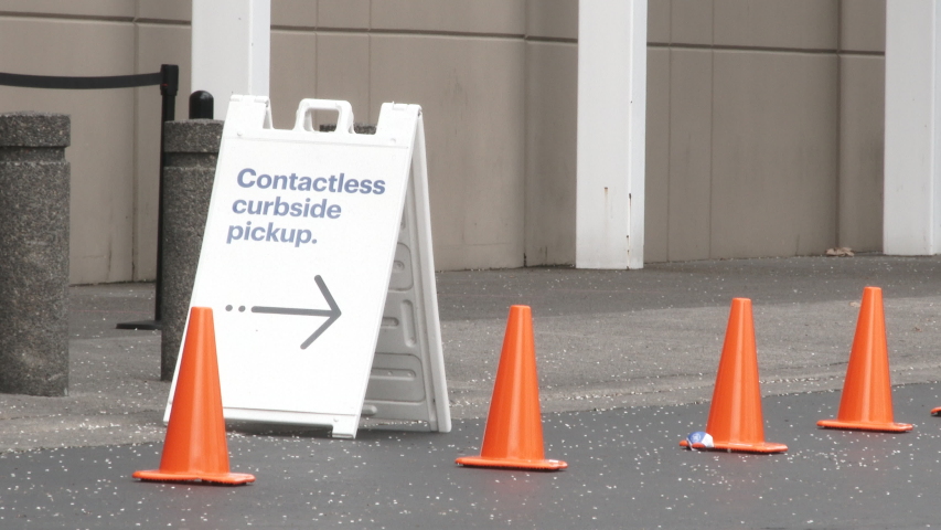 Sign reads "Contactless Curbside Pickup" outside of store with person walking by. Royalty-Free Stock Footage #1049396791
