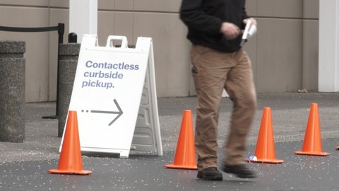 Sign reads "Contactless Curbside Pickup" outside of store with person walking by.