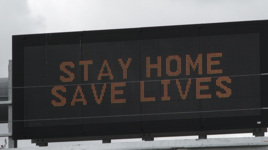 Camera zoom in and out variations on road sign reading "Stay Home, Save Lives" during the COVID-19 corona virus pandemic. Royalty-Free Stock Footage #1049399791