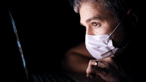 Worried man wearing face mask looks through a news site on his laptop. Latest coronavirus outbreak information related shot