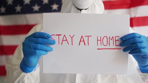 Male doctor holding a sign in his hands with an appeal to stay at home. Covid-19 coronavirus epidemic in the USA, self-isolation and quarantine