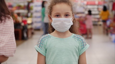 Masked child from an epidemic of coronaviruses or viruses looks at the camera amid masked people from the virus who are shopping in a panic.