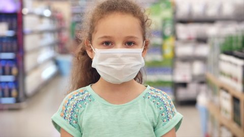 Cute little girl from an epidemic of coronaviruses or viruses looks at the camera amid masked people from the virus who are shopping in a panic. Corontin, isolation of people.