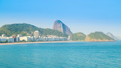Day to night sunset timelapse of the Sugarloaf mountain in Rio de Janeiro, Brazil. View of Copacabana skyline with city buildings. Ocean and beach in front, hills and mountains in background
