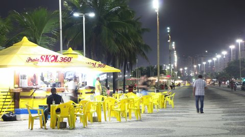 Rio de Janeiro, Brazil - March 2, 2020: Night Timelapse of street bar next to Copacabana beach with people chatting and traffic passing on the background