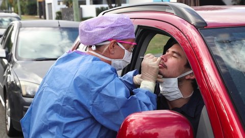 A doctor in a protective suit taking a nasal swab from a driver to test for possible coronavirus infection